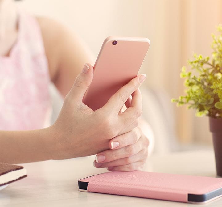 Moteris kavinėje vasarą, laikanti rožinį telefoną